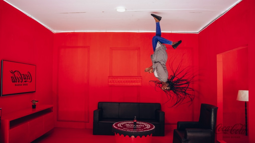 A performer suspended upside down from the ceiling of a red Coca-Cola branded room