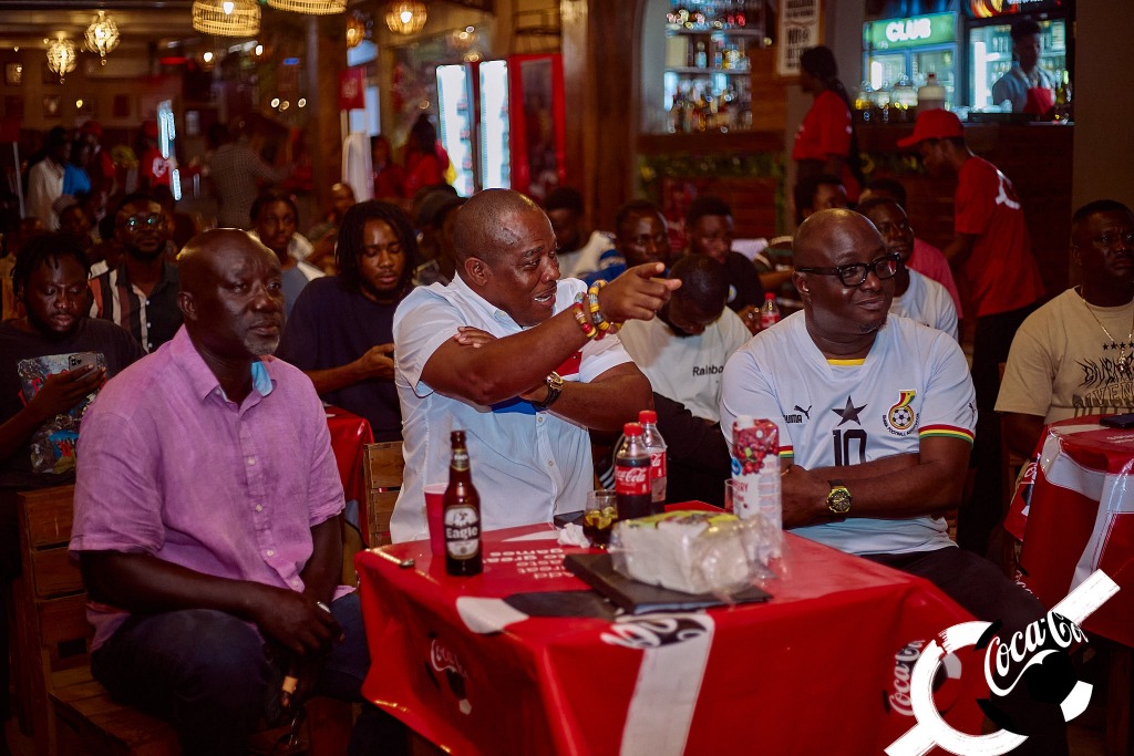 Fans watching a match together in a bar decorated with Coca-Cola branding, drinks on the tables
