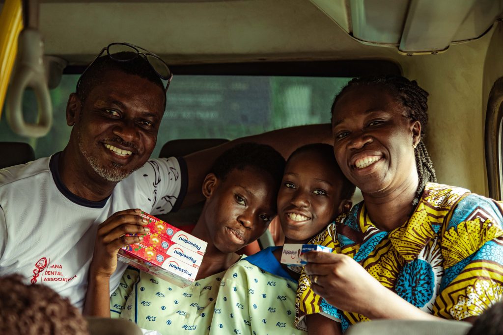 A family smiling together inside a vehicle, each holding a Pepsodent pack