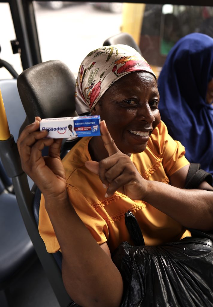 A woman in a headwrap holding up a Pepsodent pack aboard a bus