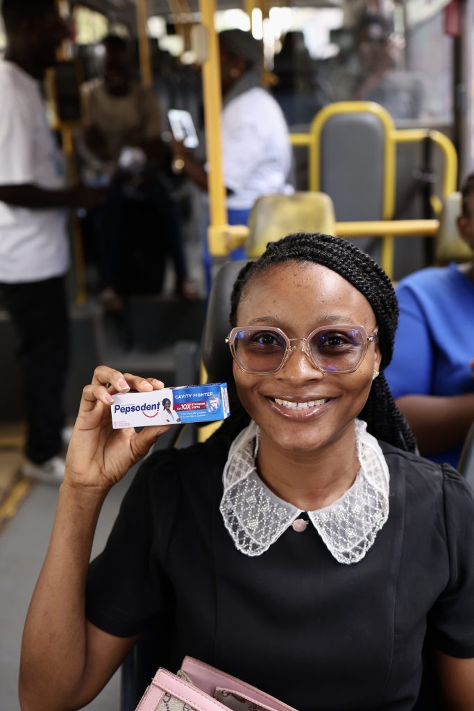 A bus passenger smiling as she holds up a pack of Pepsodent toothpaste