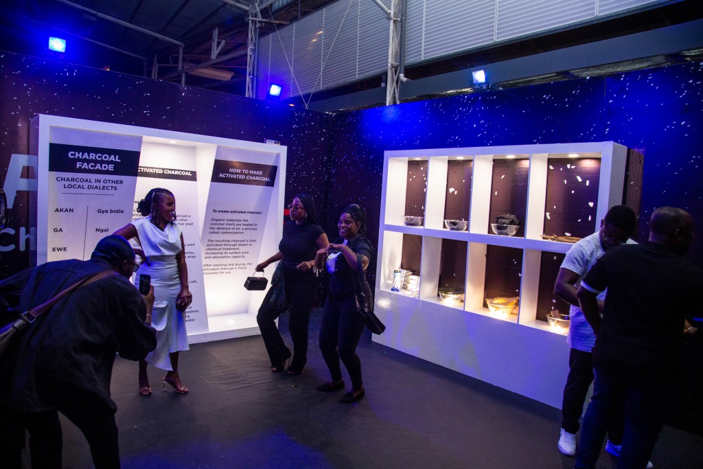 Guests exploring a lit display wall in a darkened room at the Charcoal Facade installation