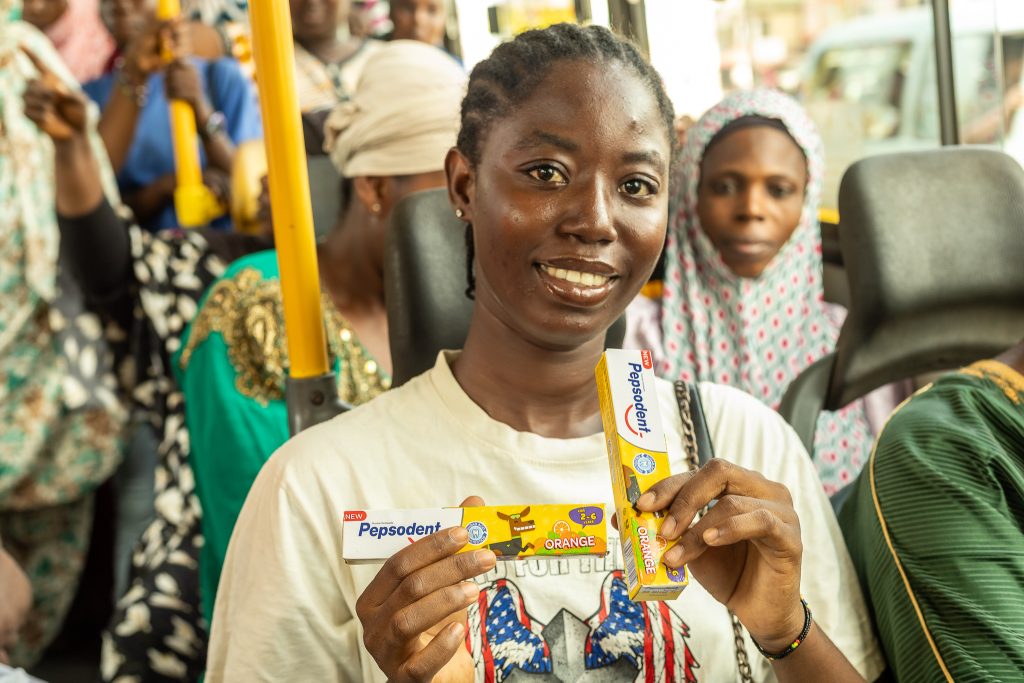 A commuter on a crowded bus holding up two packs of Pepsodent toothpaste