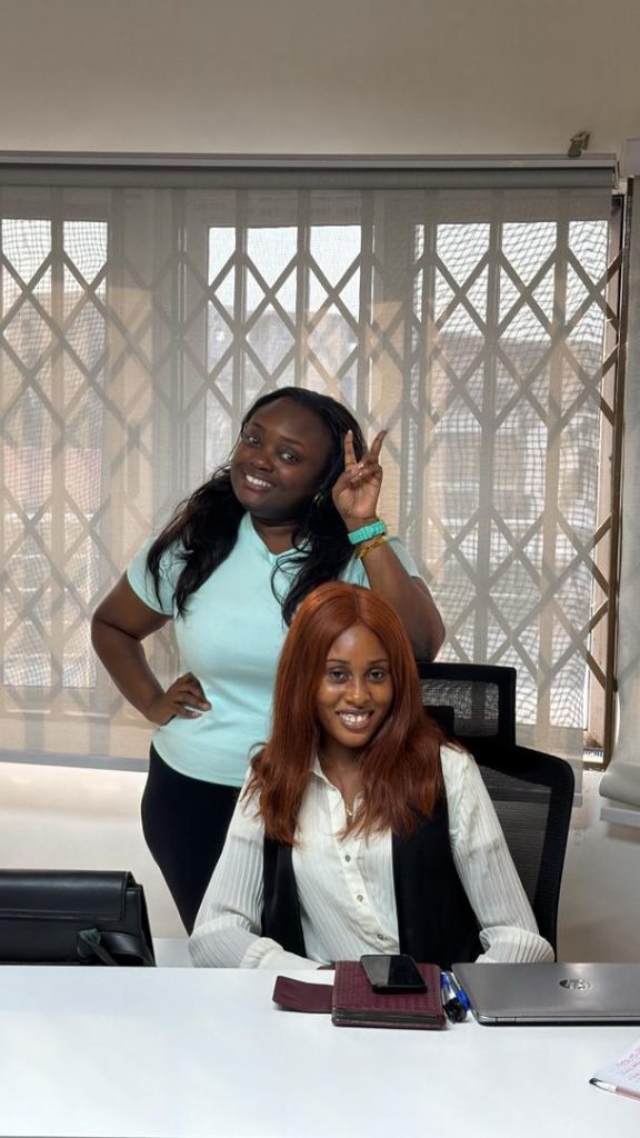 A young woman seated at the chief executive's desk while a colleague stands beside her